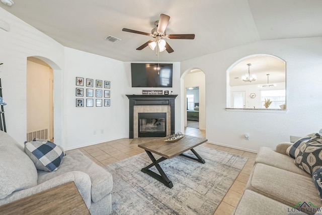 tiled living room with a tile fireplace, lofted ceiling, and ceiling fan with notable chandelier