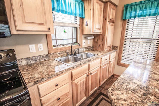 kitchen with black stove, sink, dark wood-type flooring, light stone counters, and light brown cabinetry