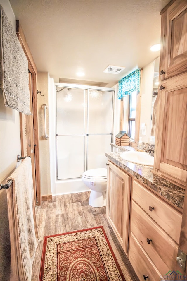 bathroom featuring toilet, vanity, a shower with shower door, and hardwood / wood-style flooring