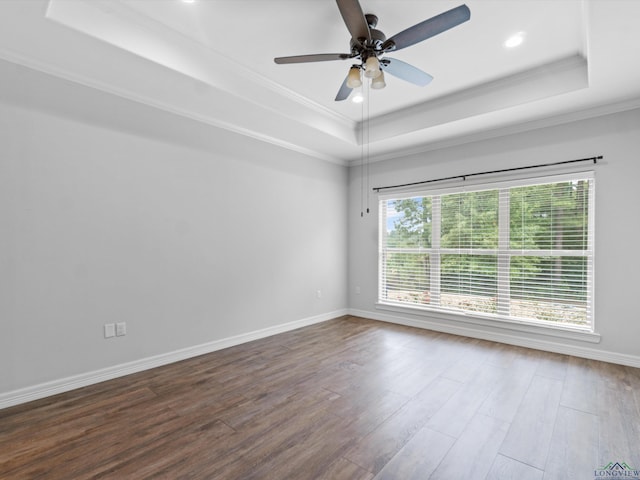 empty room featuring dark hardwood / wood-style flooring, a tray ceiling, ceiling fan, and ornamental molding