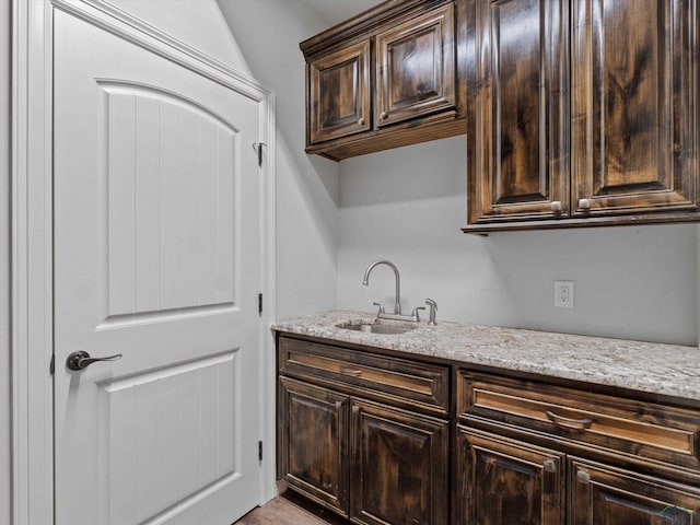 kitchen with light stone countertops, dark brown cabinetry, and sink