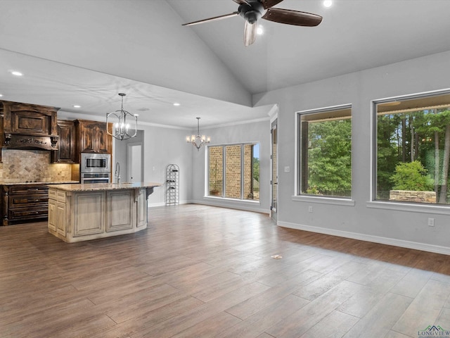 kitchen featuring backsplash, ceiling fan with notable chandelier, light hardwood / wood-style flooring, an island with sink, and appliances with stainless steel finishes