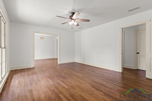 empty room with baseboards, ceiling fan, wood finished floors, and visible vents