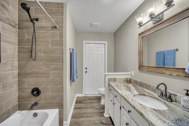 full bathroom with tiled shower / bath, wood-type flooring, vanity, toilet, and a textured ceiling