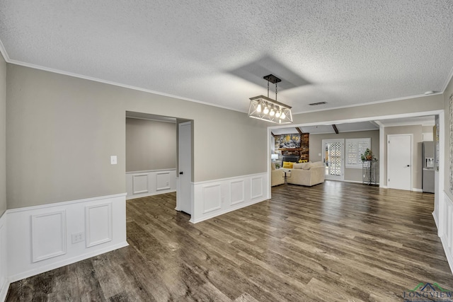 unfurnished dining area with dark hardwood / wood-style flooring, crown molding, a large fireplace, and a textured ceiling