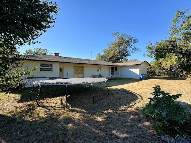 back of house with a trampoline and a lawn