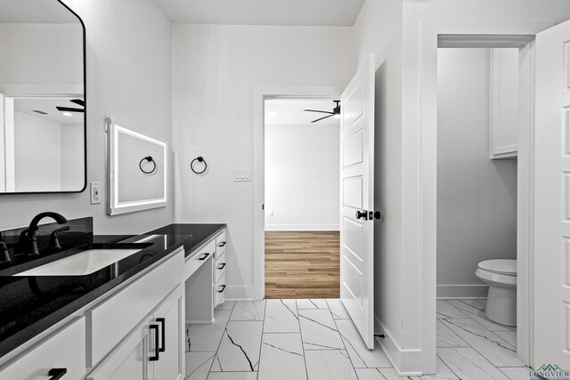 bathroom featuring ceiling fan, vanity, toilet, marble finish floor, and baseboards