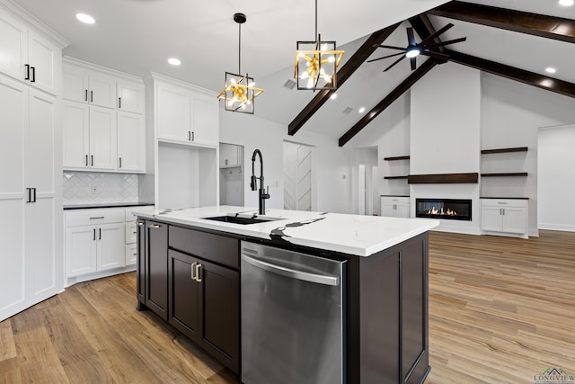 kitchen with stainless steel dishwasher, a glass covered fireplace, light wood-style floors, white cabinets, and a sink