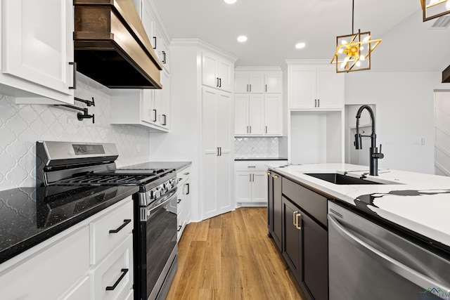 kitchen featuring wall chimney range hood, a sink, white cabinets, stainless steel appliances, and recessed lighting