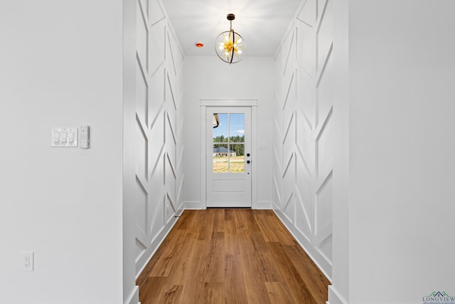 doorway to outside with baseboards, an inviting chandelier, and wood finished floors