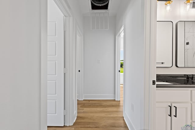 hall featuring baseboards, a sink, light wood-style flooring, and visible vents