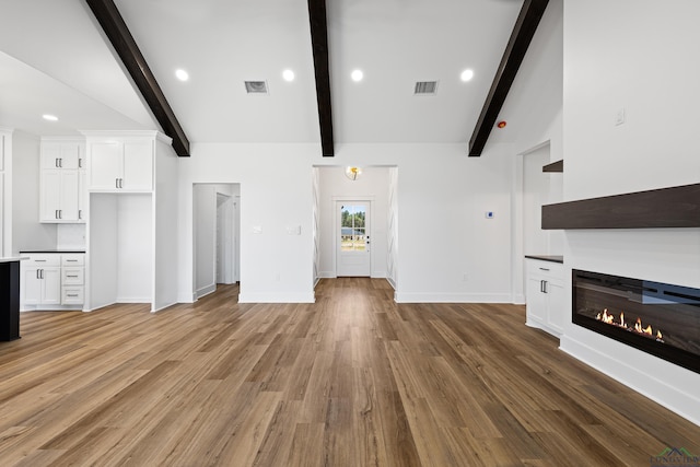 unfurnished living room featuring vaulted ceiling with beams, a glass covered fireplace, light wood-style flooring, and visible vents