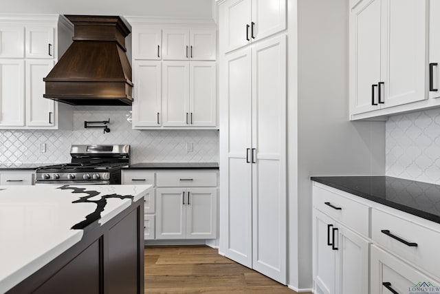 kitchen featuring stainless steel range with gas cooktop, white cabinets, decorative backsplash, and custom range hood