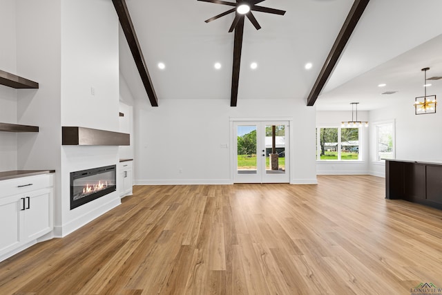 unfurnished living room featuring baseboards, lofted ceiling with beams, ceiling fan with notable chandelier, a glass covered fireplace, and light wood-style flooring
