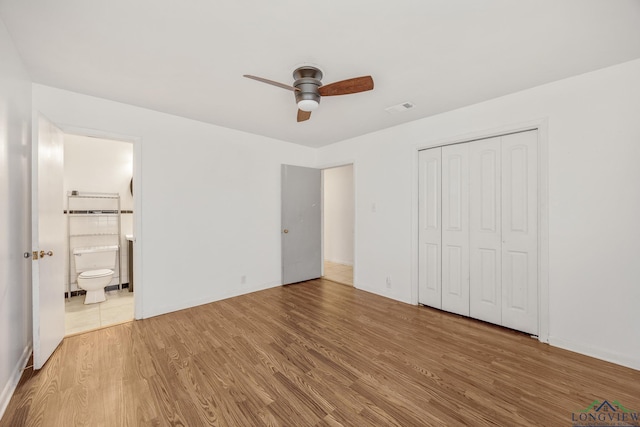 unfurnished bedroom featuring hardwood / wood-style flooring, ceiling fan, ensuite bathroom, and a closet