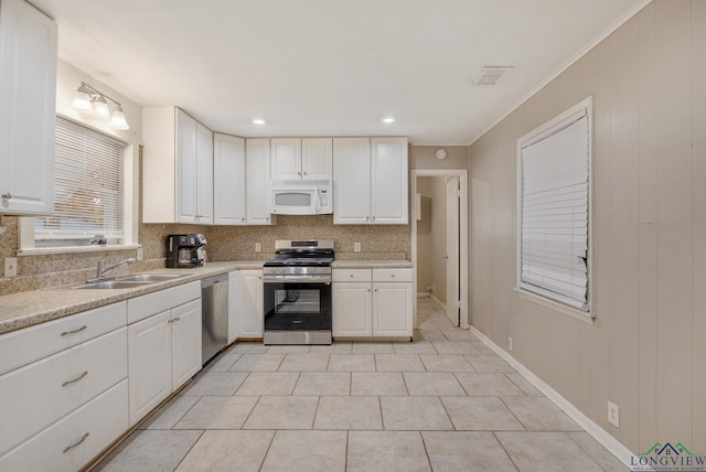 kitchen featuring sink, light tile patterned floors, tasteful backsplash, white cabinets, and appliances with stainless steel finishes