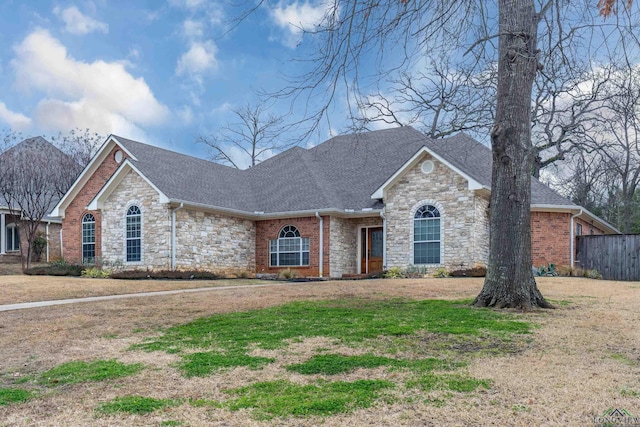 ranch-style house with a front yard, stone siding, roof with shingles, and brick siding