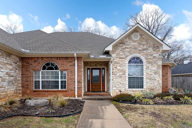 property entrance with a shingled roof, brick siding, and fence