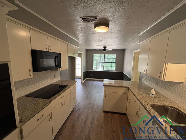 kitchen with kitchen peninsula, decorative backsplash, black appliances, and light stone counters