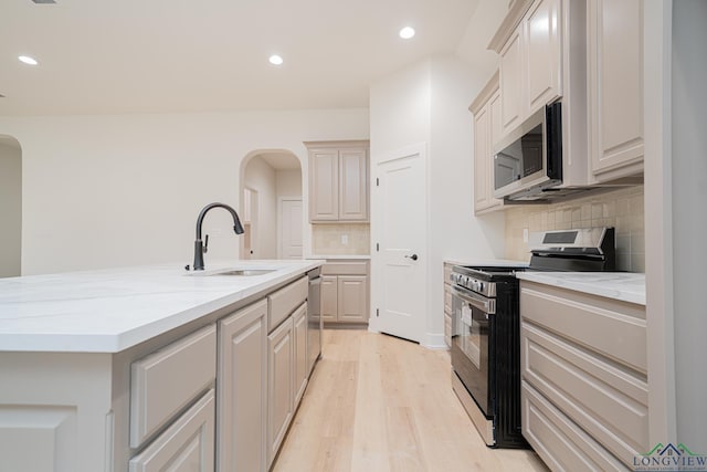 kitchen featuring sink, backsplash, stainless steel appliances, light hardwood / wood-style floors, and a center island with sink