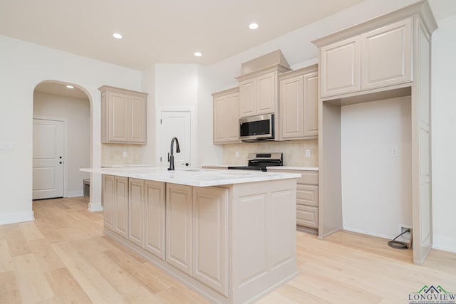 kitchen featuring sink, appliances with stainless steel finishes, tasteful backsplash, an island with sink, and light wood-type flooring