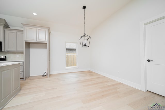 unfurnished dining area featuring lofted ceiling, a notable chandelier, and light wood-type flooring