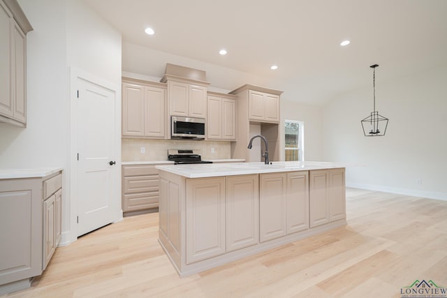 kitchen featuring appliances with stainless steel finishes, decorative light fixtures, tasteful backsplash, a kitchen island with sink, and light hardwood / wood-style flooring