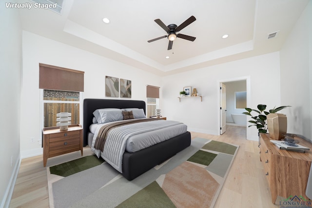 bedroom featuring ceiling fan, light wood-type flooring, and a tray ceiling