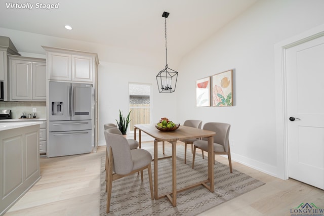 dining space with an inviting chandelier, vaulted ceiling, and light hardwood / wood-style floors