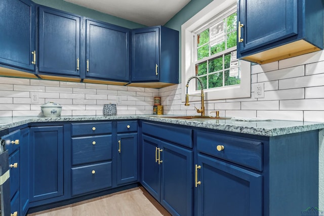 kitchen with light stone counters, a sink, blue cabinets, light wood finished floors, and backsplash