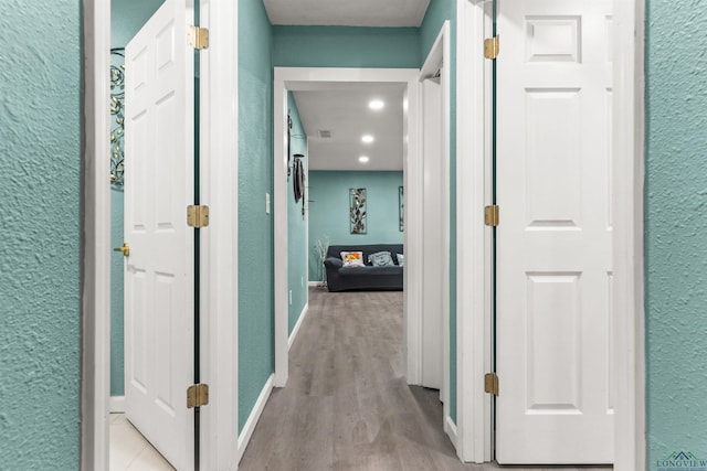 corridor with wood finished floors, a textured wall, visible vents, and baseboards