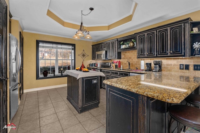 kitchen with light stone counters, a center island, a tray ceiling, pendant lighting, and stainless steel appliances