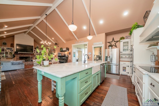 kitchen with sink, a brick fireplace, lofted ceiling with beams, a center island with sink, and appliances with stainless steel finishes