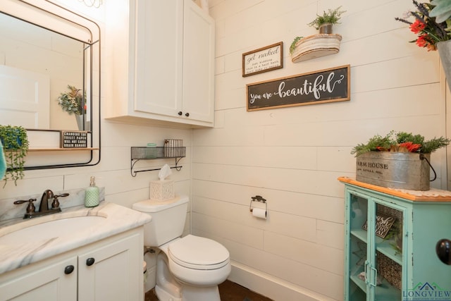 bathroom featuring wooden walls, vanity, and toilet