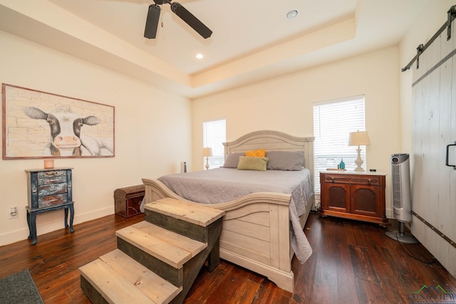 bedroom featuring ceiling fan, dark hardwood / wood-style floors, a raised ceiling, and a barn door