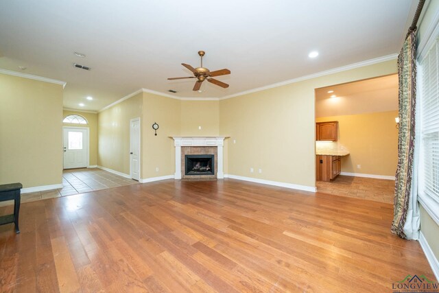 unfurnished living room featuring crown molding, light wood-type flooring, a tile fireplace, and baseboards