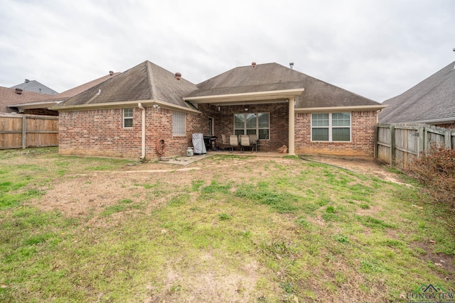 rear view of property with a fenced backyard, brick siding, a yard, roof with shingles, and a patio area