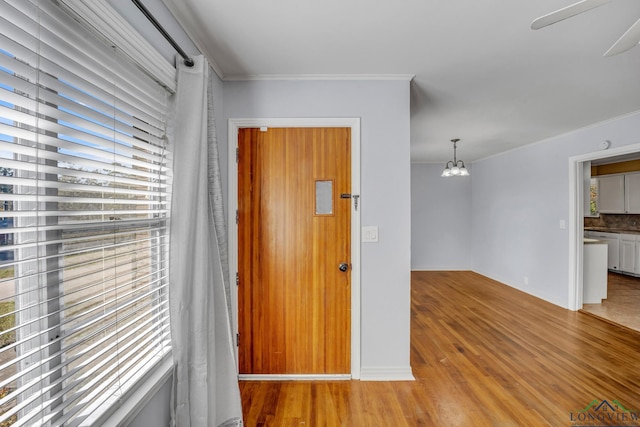 entrance foyer featuring ceiling fan with notable chandelier, wood-type flooring, and crown molding