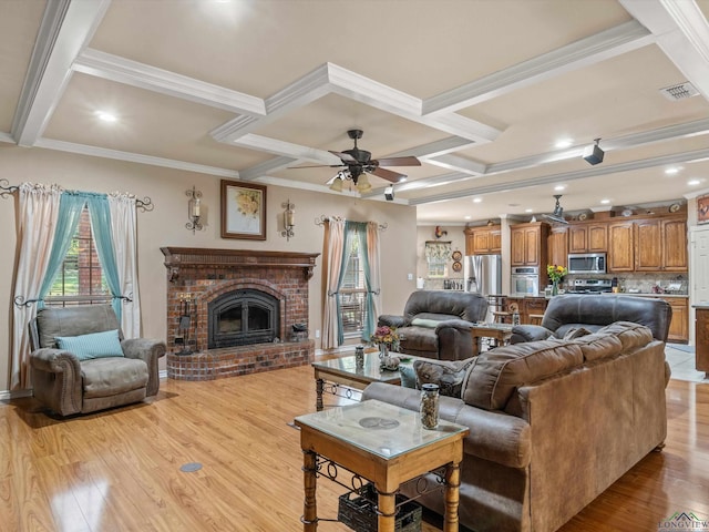 living room with coffered ceiling, ceiling fan, ornamental molding, light wood-type flooring, and a fireplace