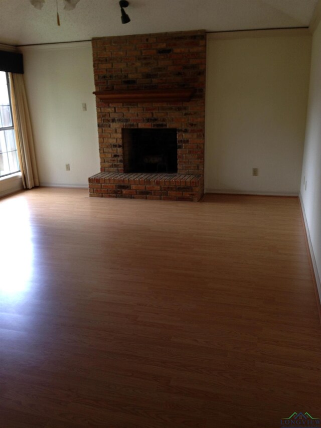 1204 Brandywine Dr, Longview, TX 75601 - unfurnished living room featuring wood finished floors, a ceiling fan, and a brick fireplace