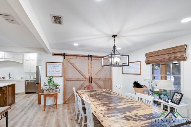 dining space with sink, light hardwood / wood-style flooring, a barn door, and a chandelier