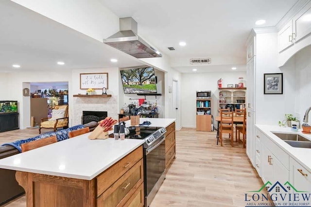 kitchen featuring sink, white cabinetry, a center island, stainless steel appliances, and wall chimney range hood