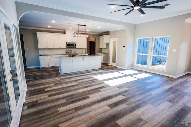 kitchen featuring appliances with stainless steel finishes, dark wood-type flooring, a center island with sink, white cabinetry, and hanging light fixtures