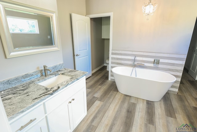 bathroom with hardwood / wood-style floors, vanity, a bathtub, toilet, and tile walls