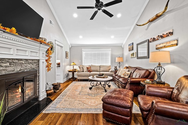 living room featuring dark hardwood / wood-style floors, a stone fireplace, crown molding, and vaulted ceiling