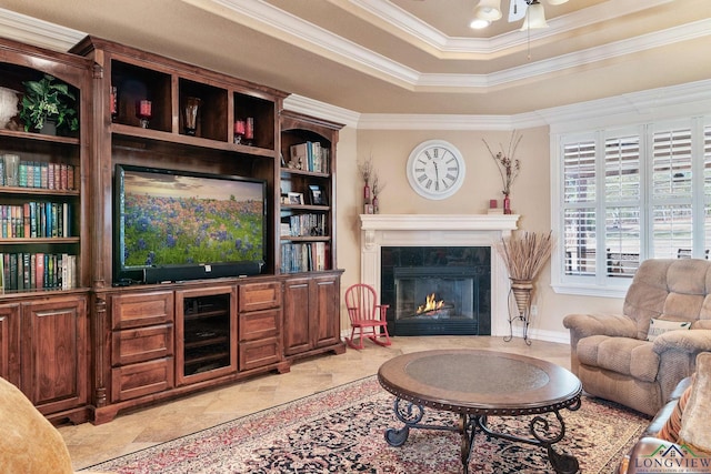 living area with a ceiling fan, a tray ceiling, crown molding, and a tiled fireplace