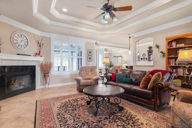 living area featuring baseboards, a raised ceiling, ceiling fan, ornamental molding, and a high end fireplace