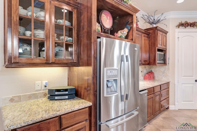 kitchen with decorative backsplash, glass insert cabinets, brown cabinets, light stone counters, and stainless steel appliances