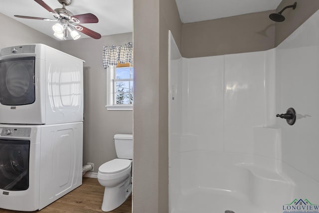 bathroom with toilet, hardwood / wood-style floors, a shower, stacked washer and dryer, and ceiling fan