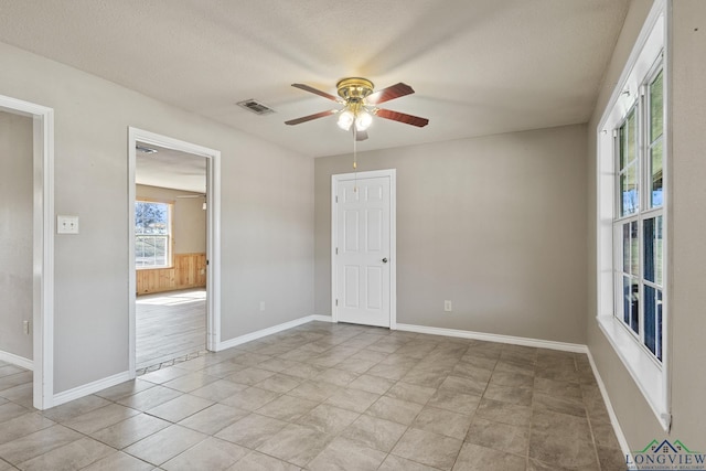 empty room with ceiling fan, wood walls, a textured ceiling, and light tile patterned flooring